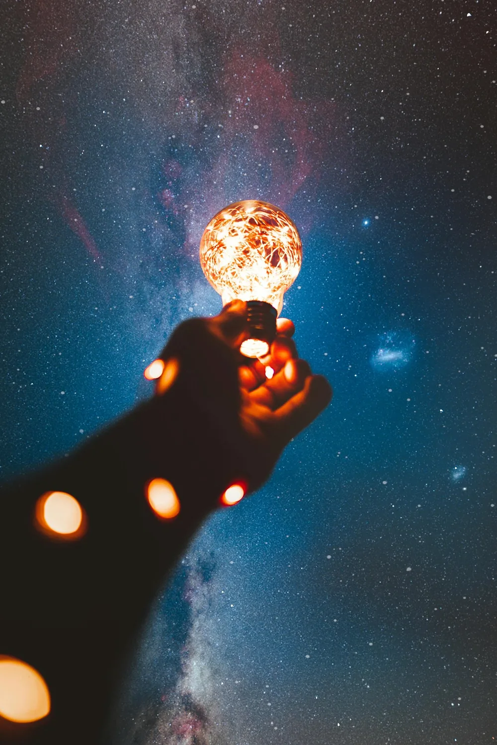 Une main tient une ampoule lumineuse sous un ciel étoilé